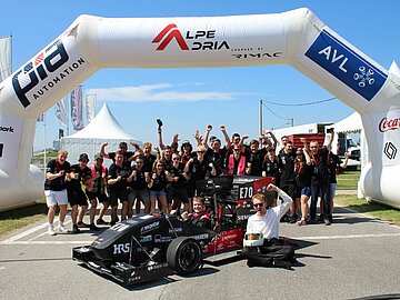 Das jubelnde Team CURE mit Rennwagen in der Mitte auf der Rennstrecke der Alpe Adria in Kroatien.