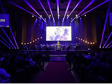 Blick aus dem Zuschauersaal auf die lila und gold beleuchtete Bühne des Mozartsaals, auf der SAP Sinfonieorchester spielt.