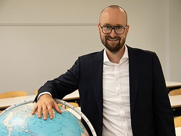 Porträt Prof. Stenger, der sich an einen Globus lehnt, in einem Hörsaal der DHBW Mannheim.