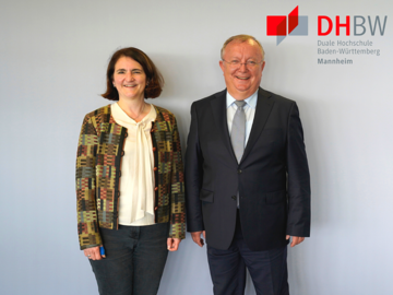 Porträt Dr. Elke Schwing und Prof. Dr. Georg Nagler mit Logo der DHBW Mannheim im Hintergrund