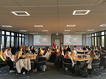 Das von Prof. Kathrin Kölbl organisierte Angebot im Rahmen der Frauenwirtschaftstage begeisterte DHBW-Studentinnen wie -Studenten. Eine Zuhörerschaft von mehr als 30 Personen an 4 Gruppentischen blickt auf die Referentin und deren Powerpoint-Präsentation.