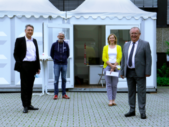 Vier Leute stehen vor einem weißen Zelt im Hof des Campus