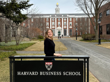 Christin Pohl vor einem Schild mit der Aufschrift Harvard Business School, dahinter die Hauptbibliothek (Baker Library) 