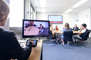 Personengruppe an einem runden Tisch im Focus Grop Lab der DHBW Mannheim werden von einer Frau über Monitor beobachtet