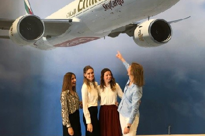 Vier Studentinnen vor einem Flugzeugplakat der Fluggesellschaft Emiratesin Dubai 