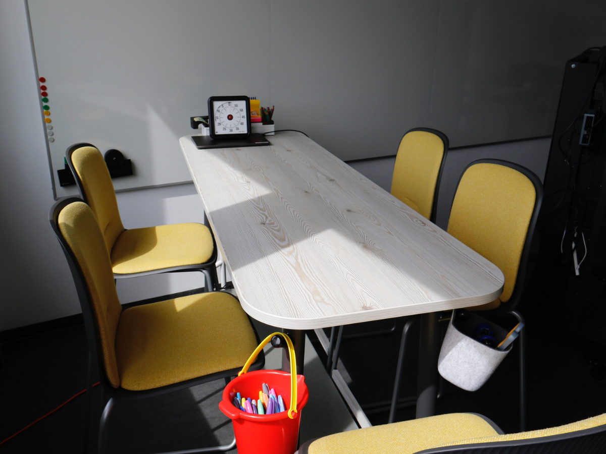 5 gelbe Barhocker an Tisch, der mit Bastelmaterialien ausgestattet ist. 